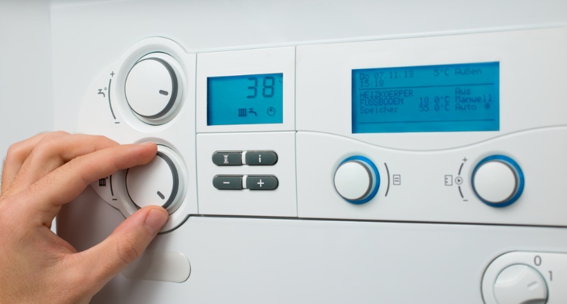 Main réglant le thermostat d'une chaudière murale pour optimiser la température de l'eau chaude